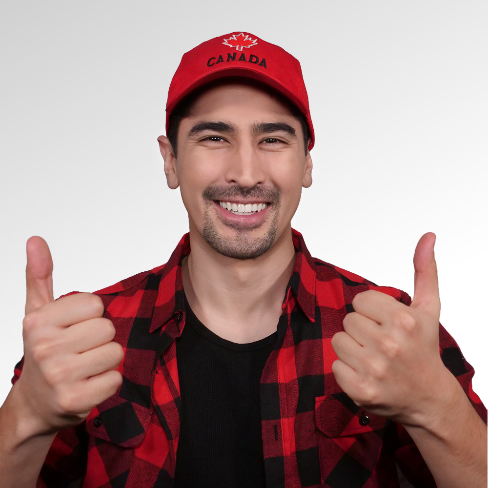 English language coach James Bong smiles at the camera with both thumbs up, wearing a Canadian cap and a buffalo plaid shirt.
